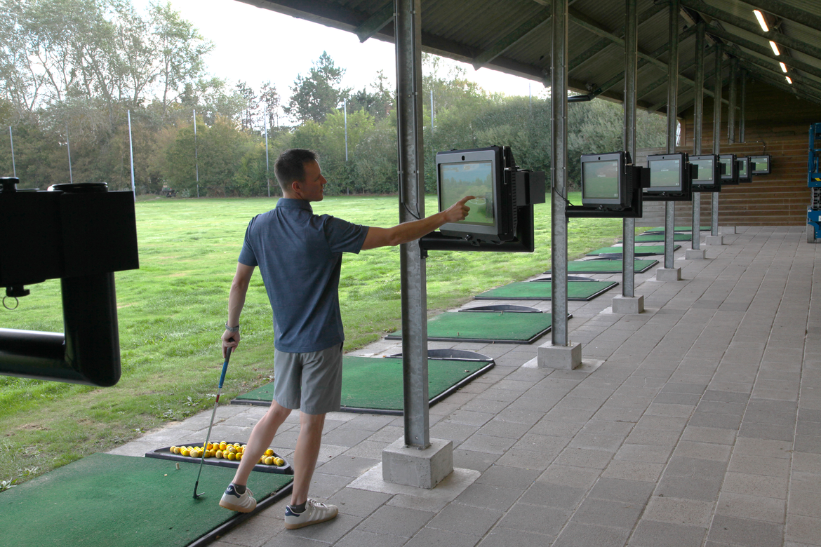 een golfer bedient het trackman scherm op de driving range