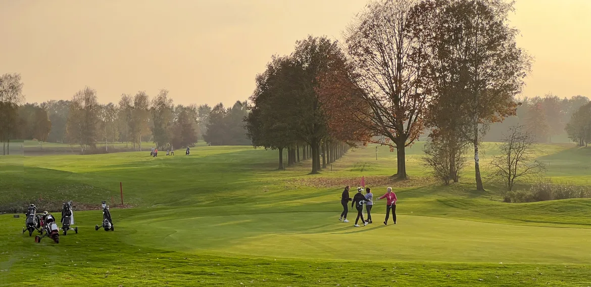 4 dames golfers op de green van hole 9 met laagstaande zon