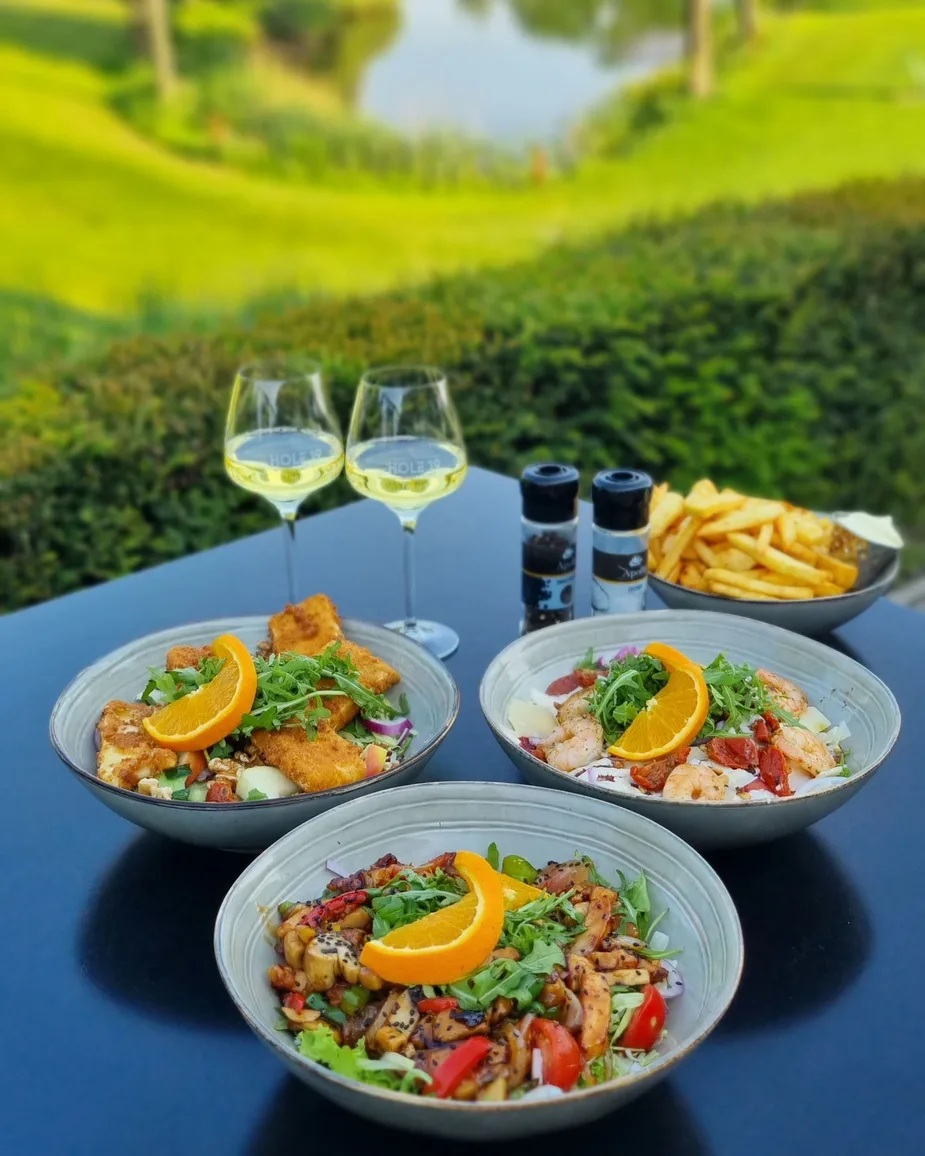 2 borden maaltijdsalade, 2 glazen witte wijn en friet op het terras van Hole 19